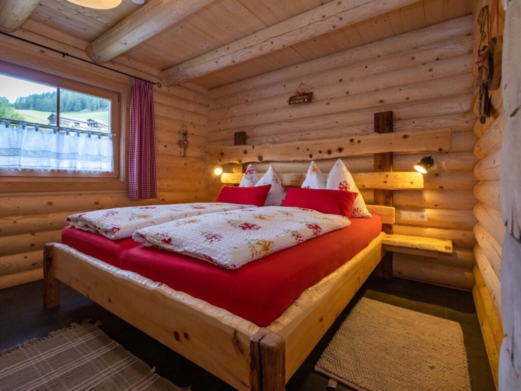 Schlafzimmer der Alm mit Holzwänden, Doppelbett und Leselampen, sowie Ausblick auf die umgebende Landschaft.